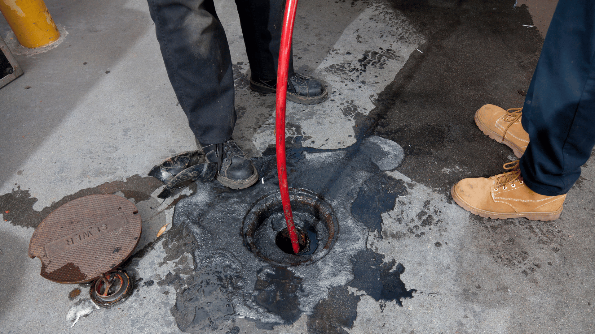 A manhole cover with a red hose sticking out of it.