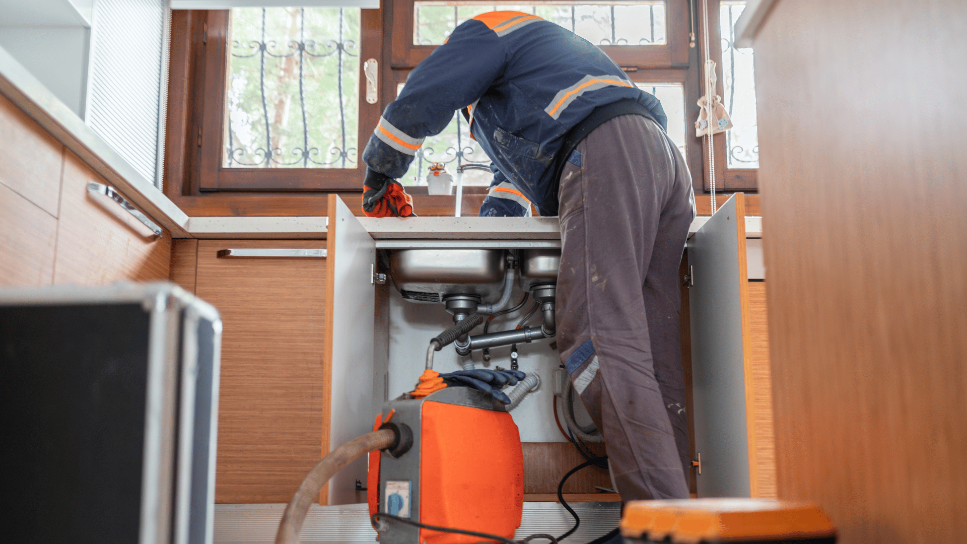A plumber is fixing a sink in a kitchen with a vacuum cleaner.