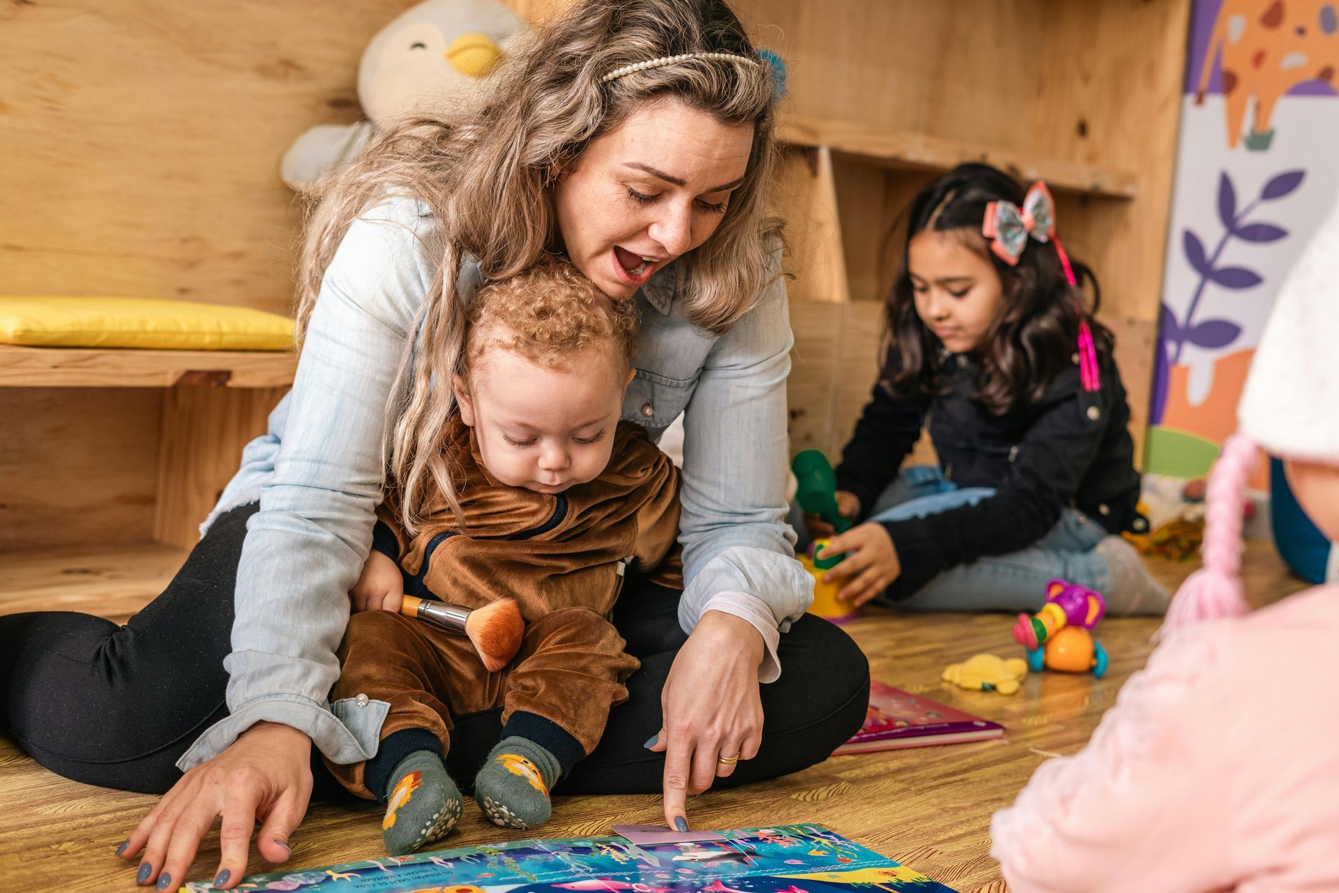 Woman reading to a toddler, children playing in a brightly lit playroom.
