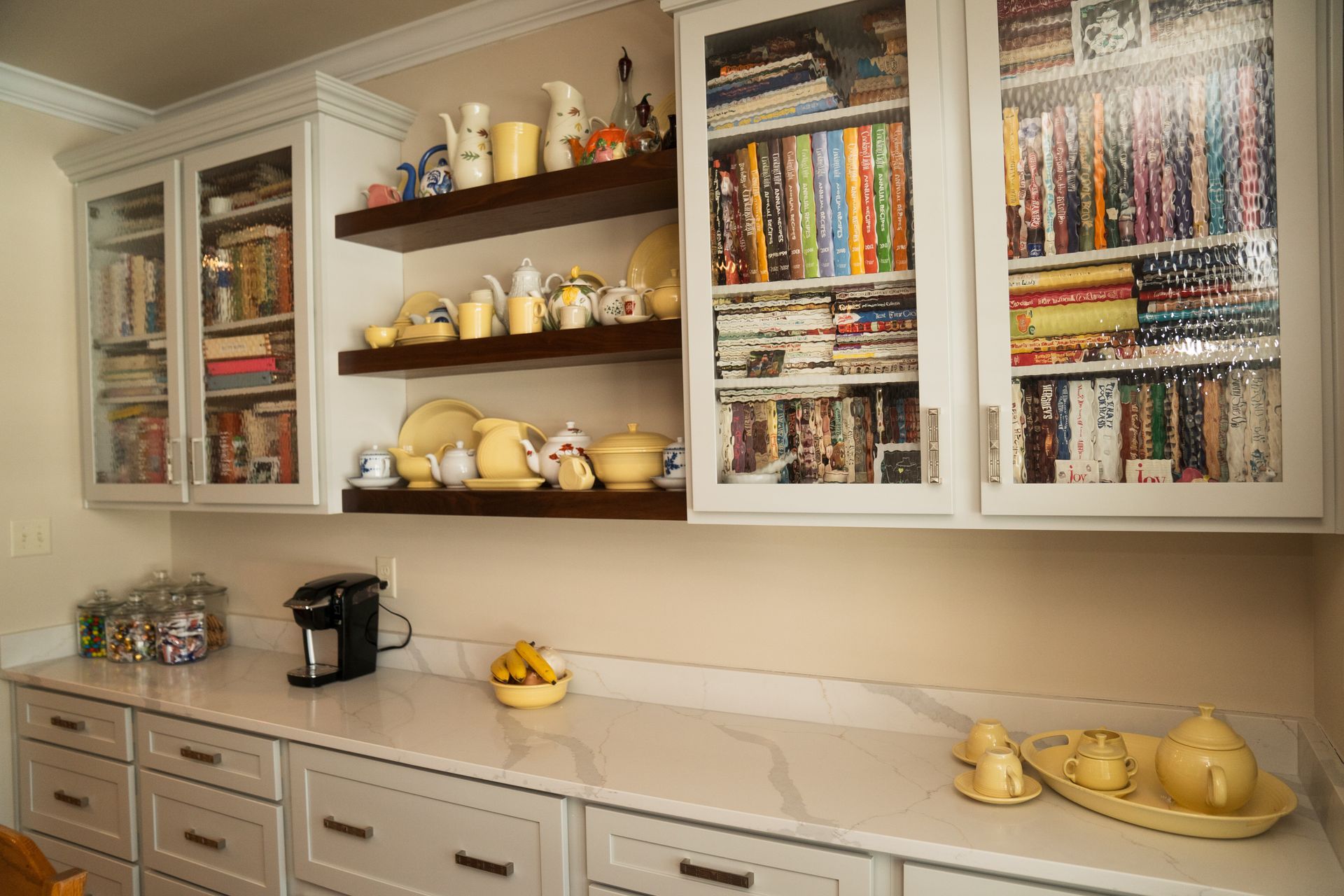 A kitchen with white cabinets, white counter tops, and glass doors.