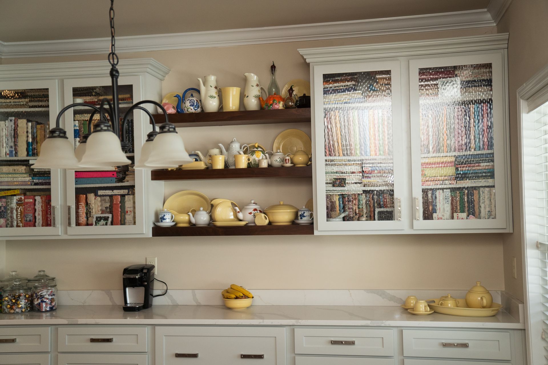 A kitchen with white cabinets and shelves filled with dishes and books.