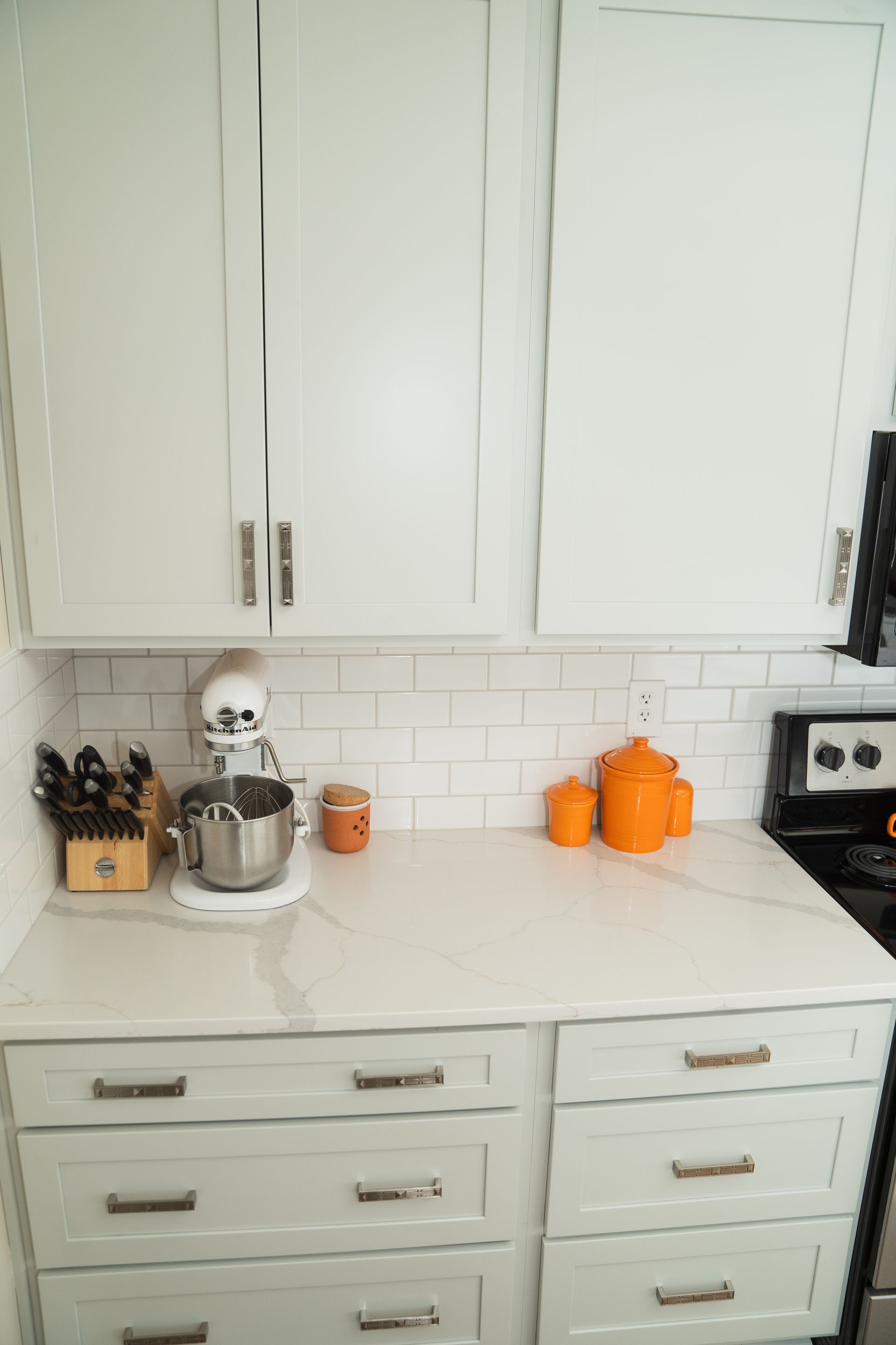 A kitchen counter with white cabinets, drawers, a mixer, and a stove.