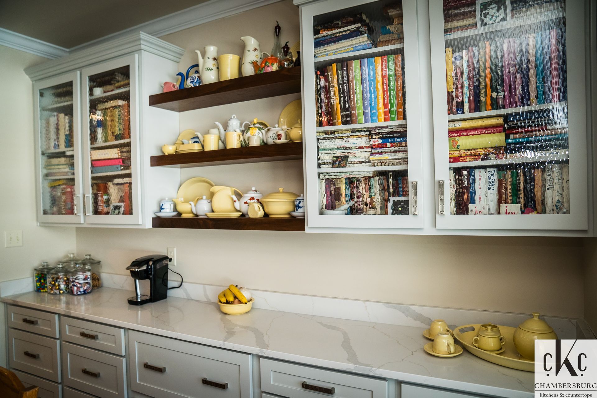 A kitchen with white cabinets, white counter tops, and glass doors.