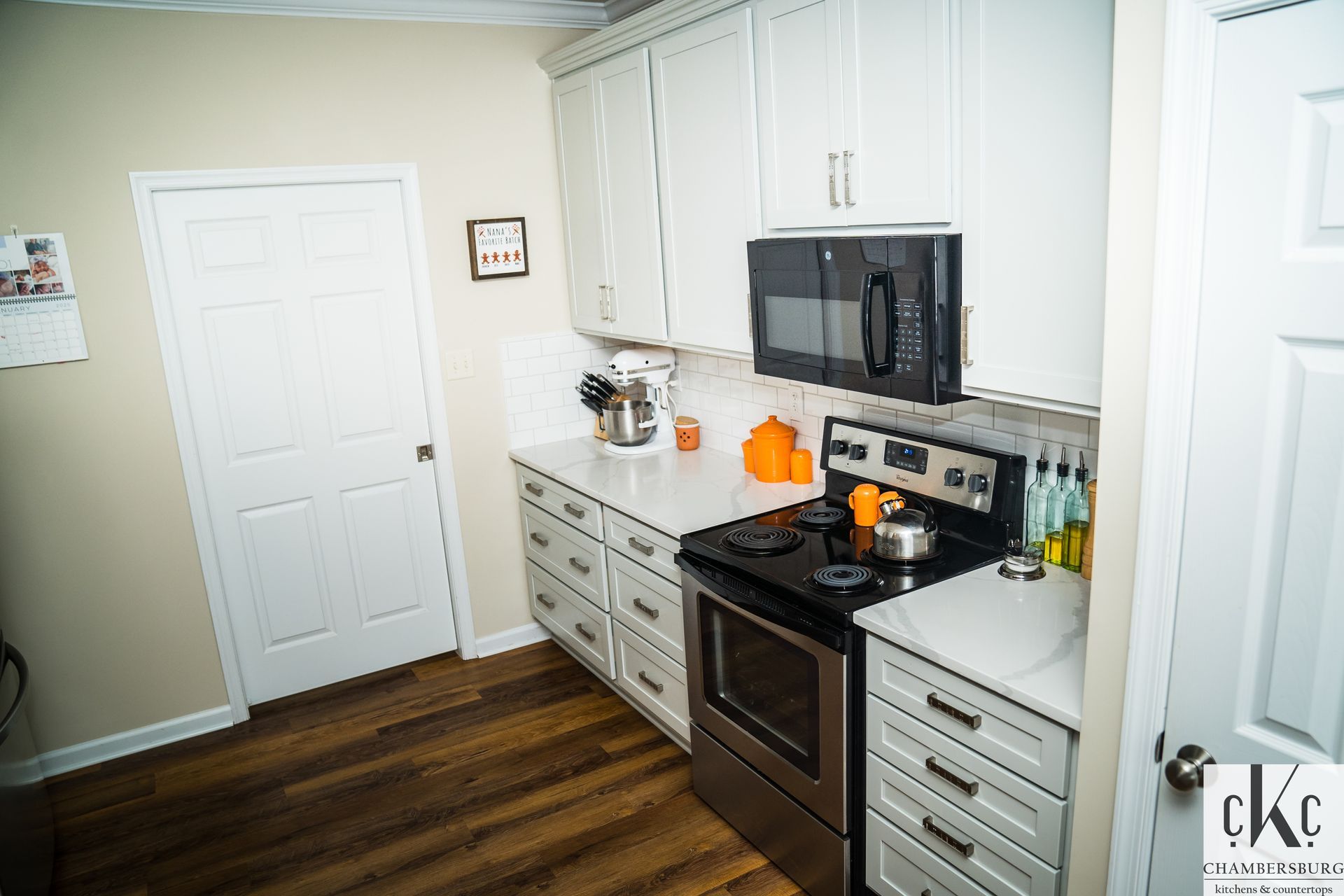 A kitchen with white cabinets, a stove, a microwave, and a door.