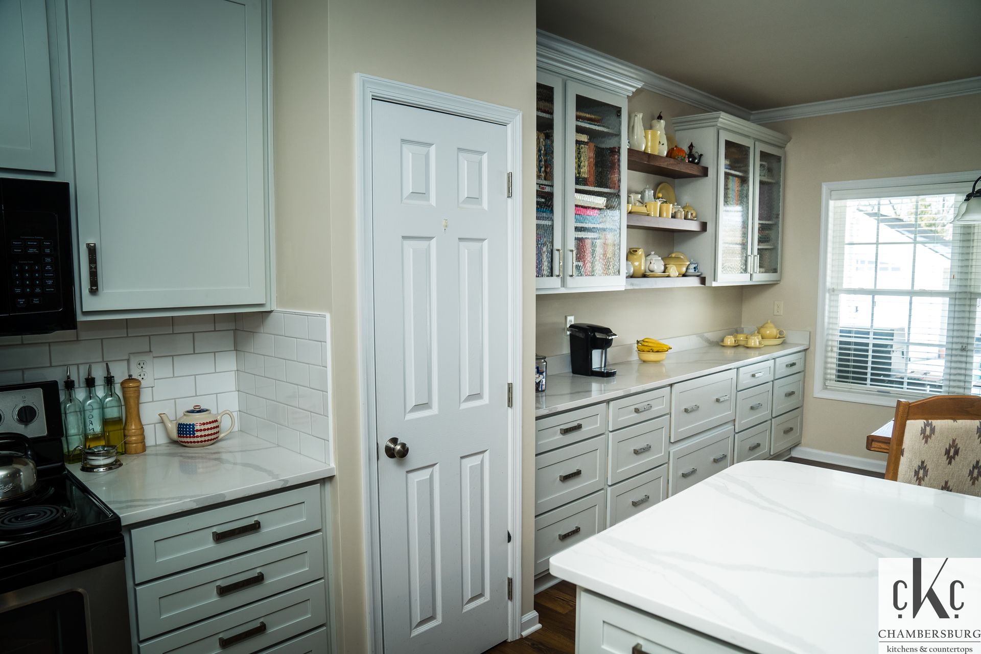 A kitchen with white cabinets, white counter tops, and a large island.