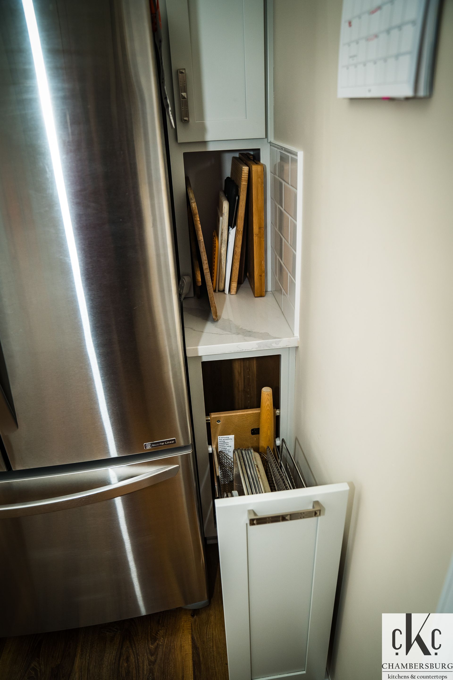 A kitchen with a stainless steel refrigerator and a drawer filled with knives and utensils.