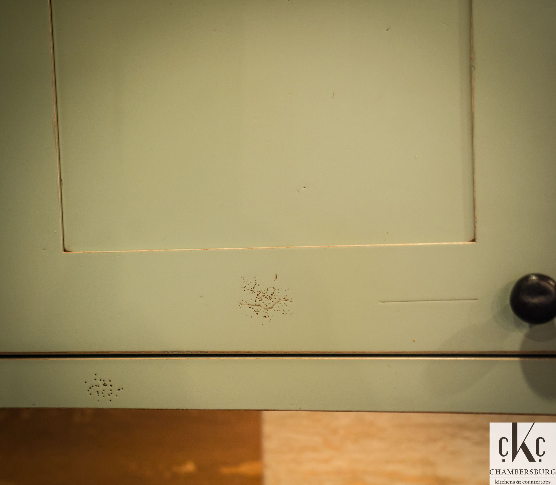 A close up of a green cabinet with a black knob.