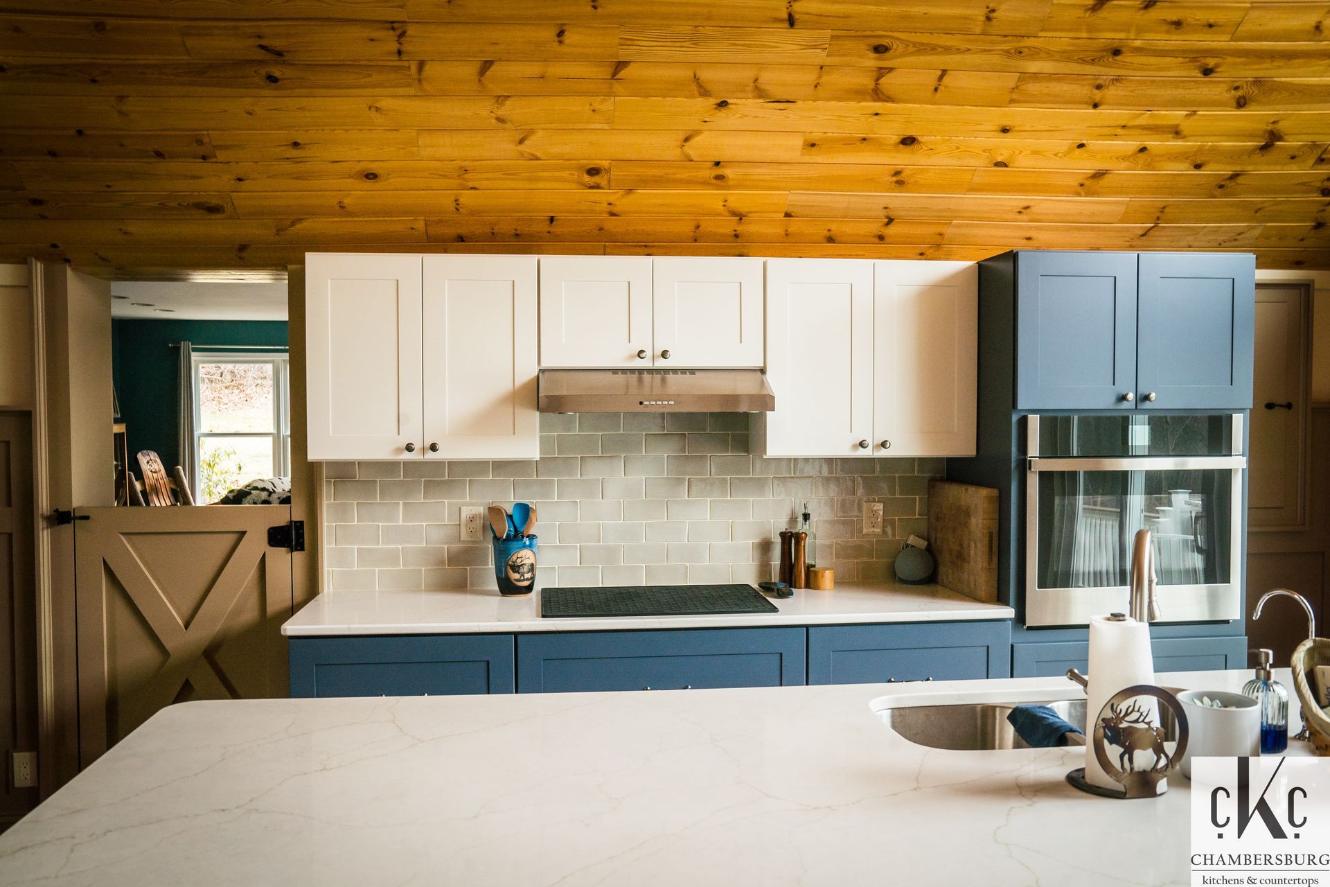 A kitchen with blue cabinets and white counter tops and a wooden ceiling.