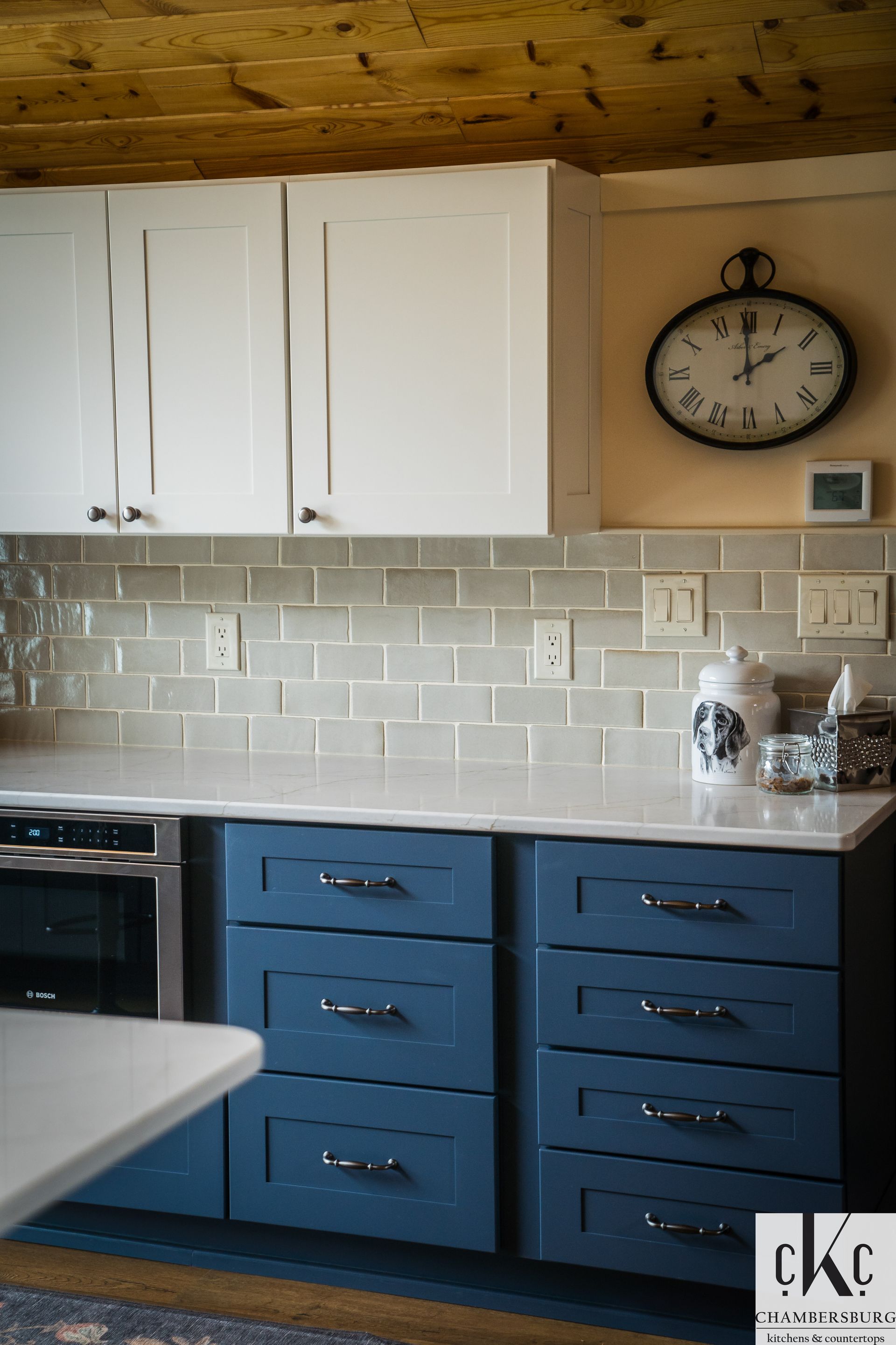 A kitchen with white cabinets and blue drawers and a clock on the wall