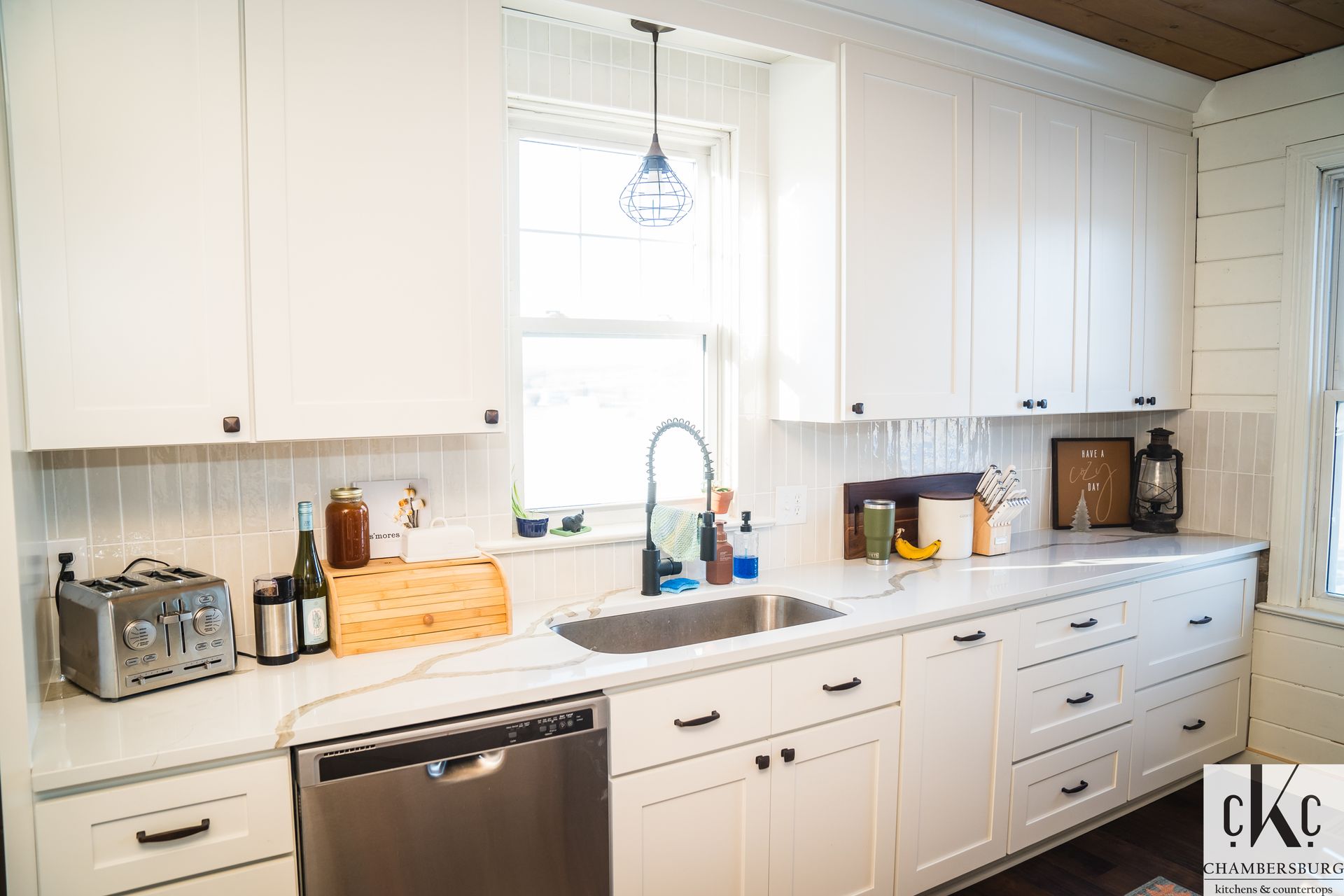 A kitchen with white cabinets, a sink, a dishwasher, and a window.