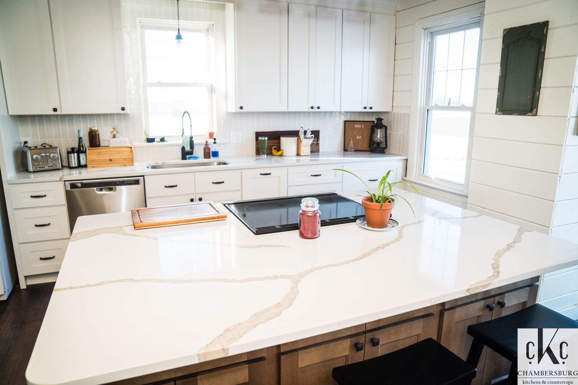 A kitchen with white cabinets and a large island with a stove top oven.