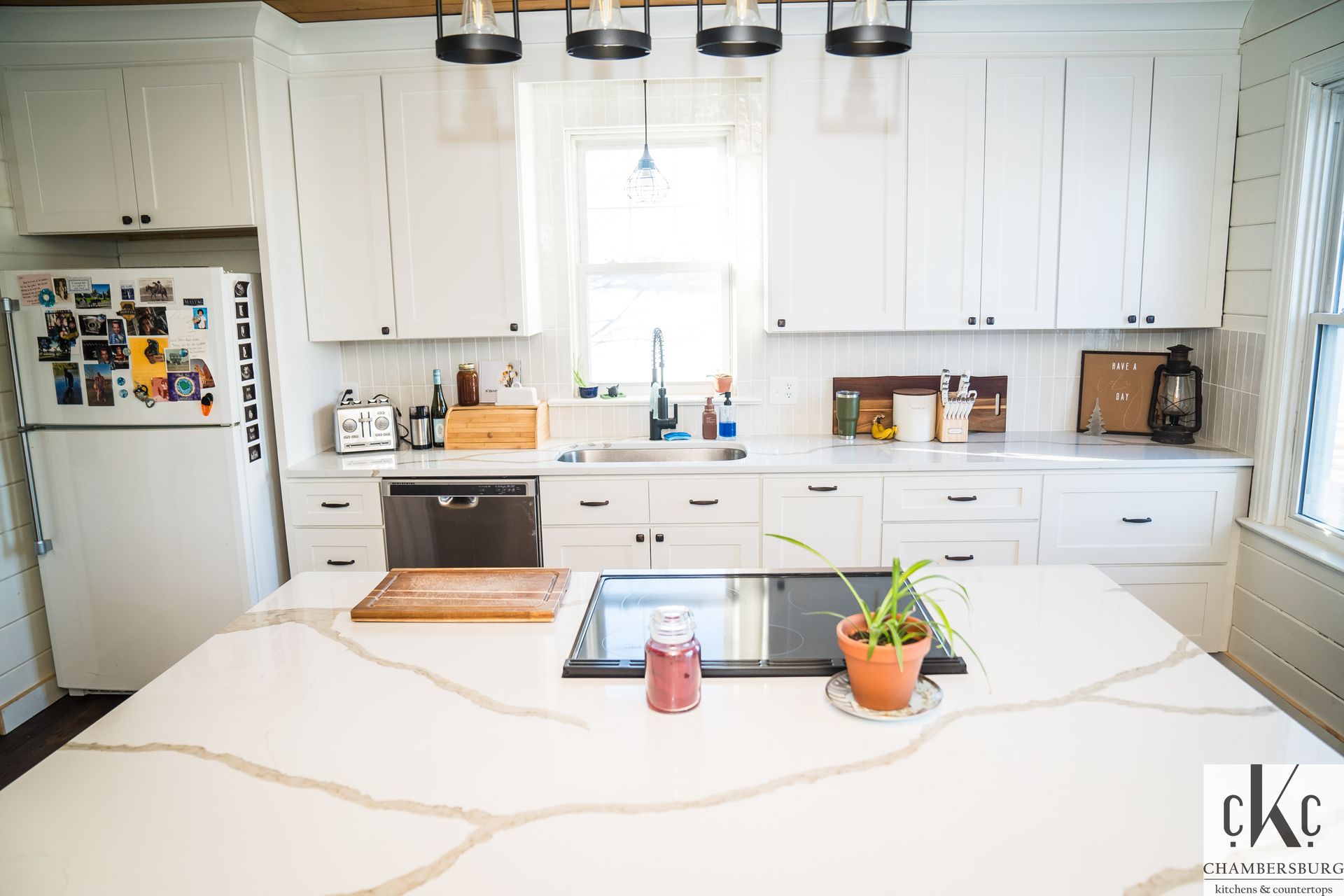 A kitchen with white cabinets, a stove, a refrigerator, a sink, and a large island.