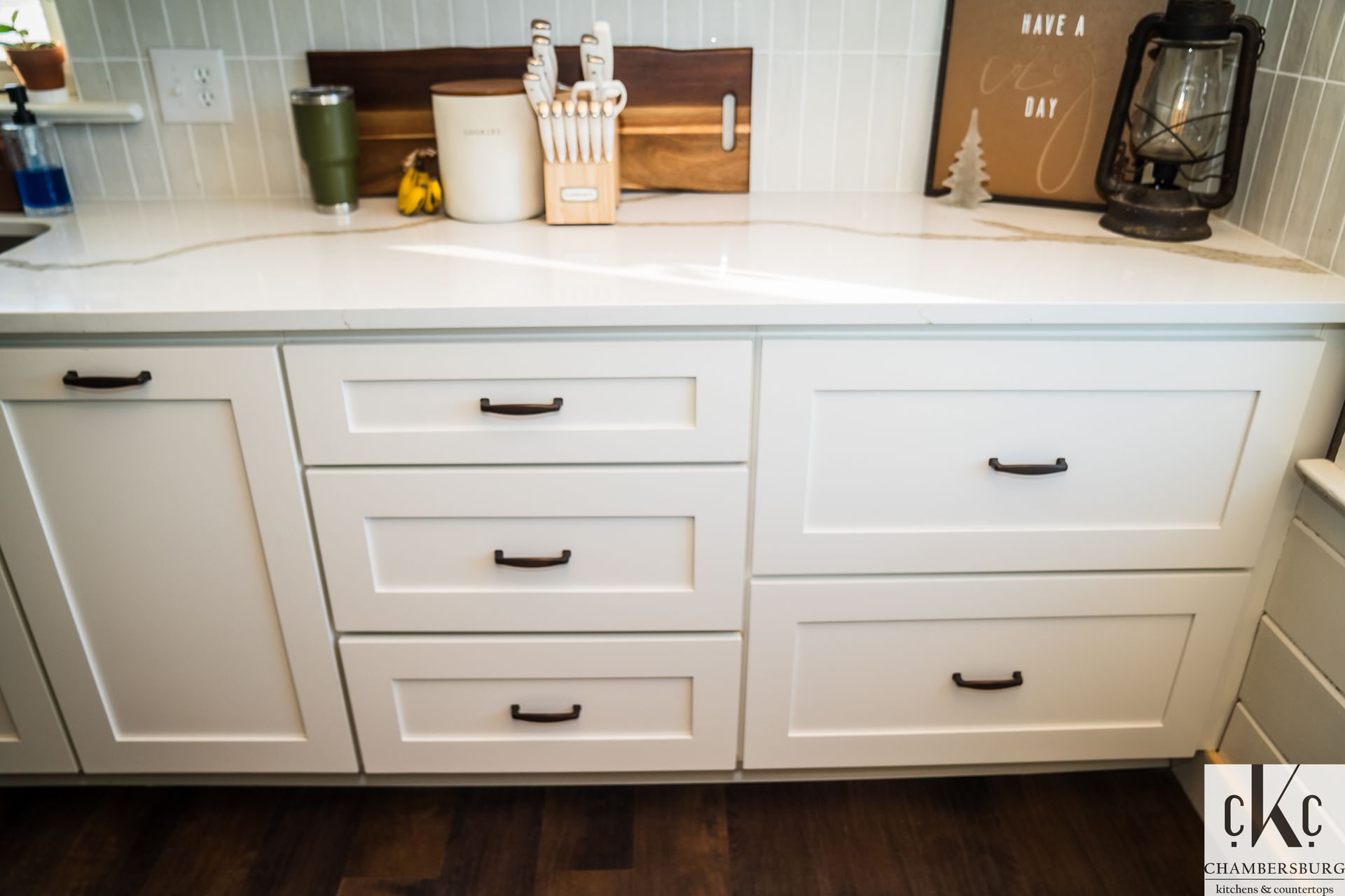 A kitchen counter with white cabinets and black handles.