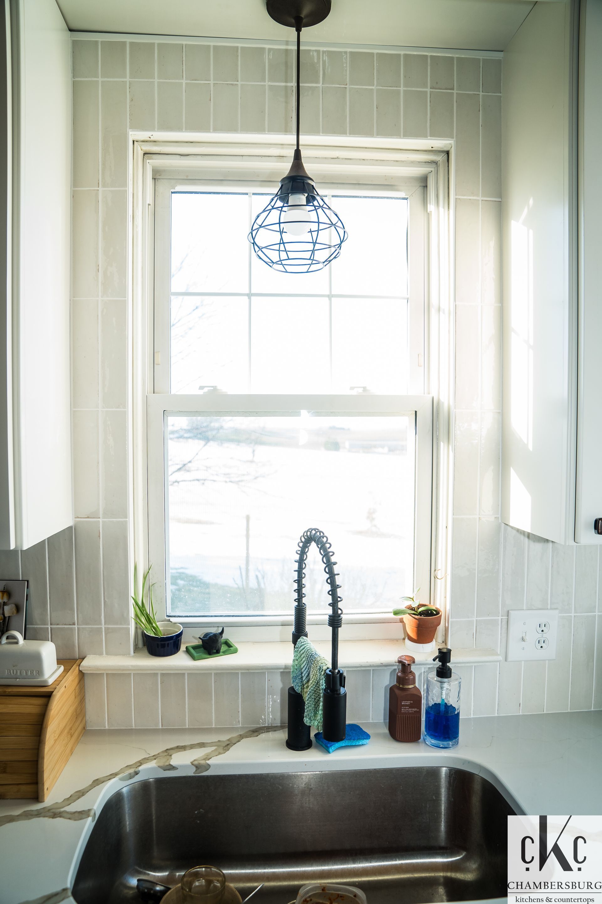 A kitchen with a sink and a window with a light hanging from the ceiling.