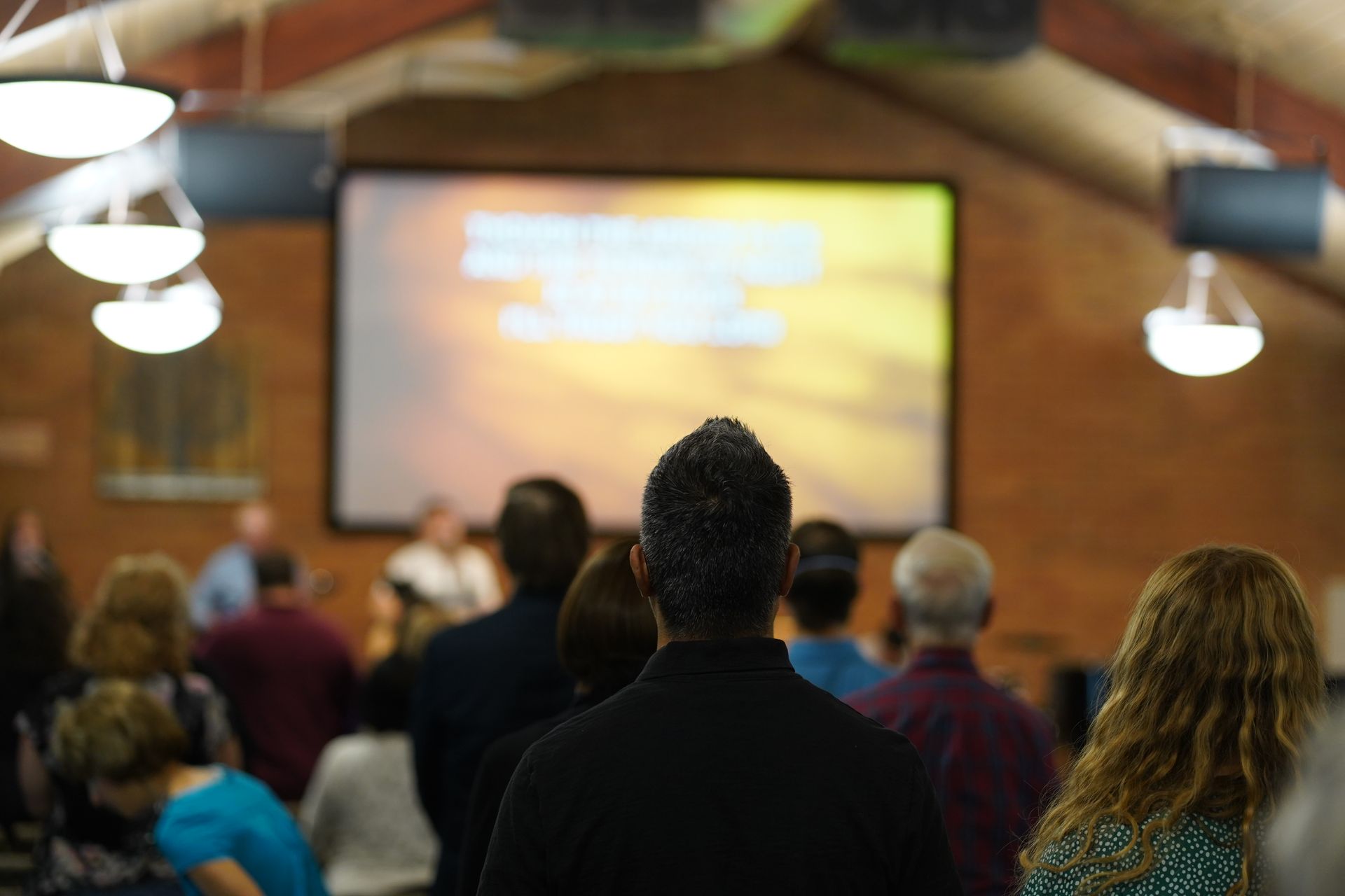 A group of people are watching a church service on a large screen.