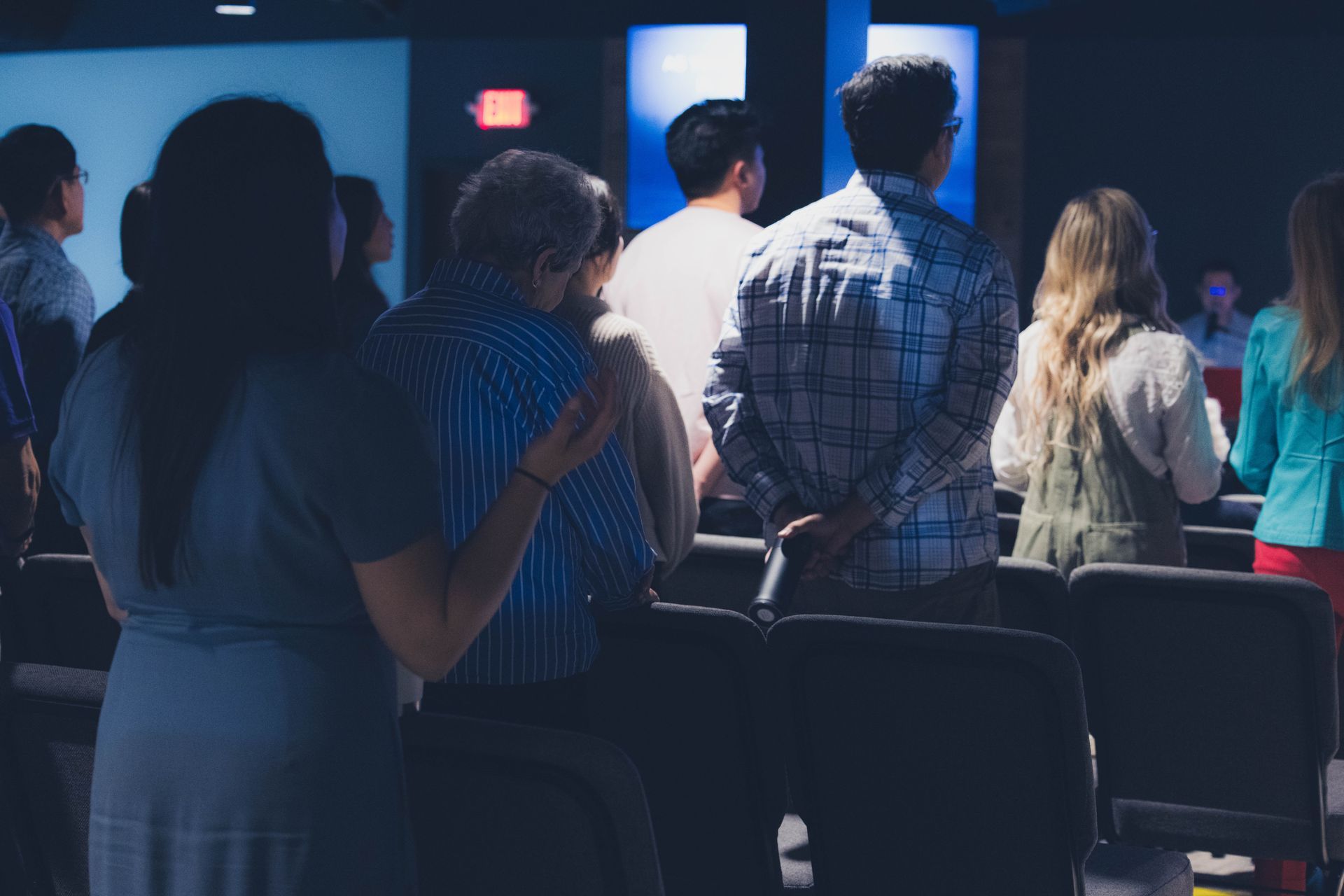 People standing and praying in a church, facing forward.  Soft lighting, blue tones.