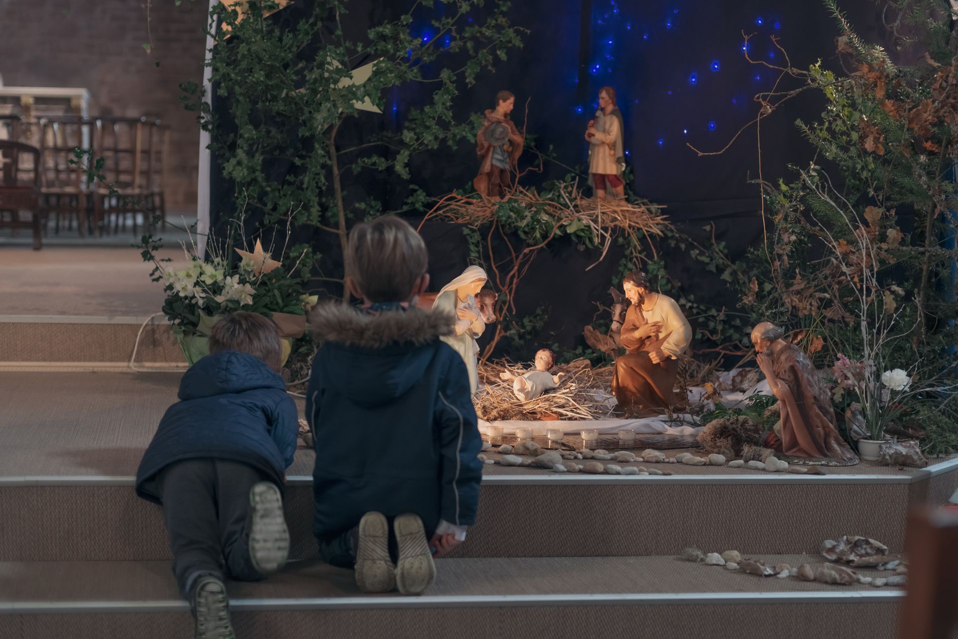 Two children are sitting on the steps of a church looking at a nativity scene.