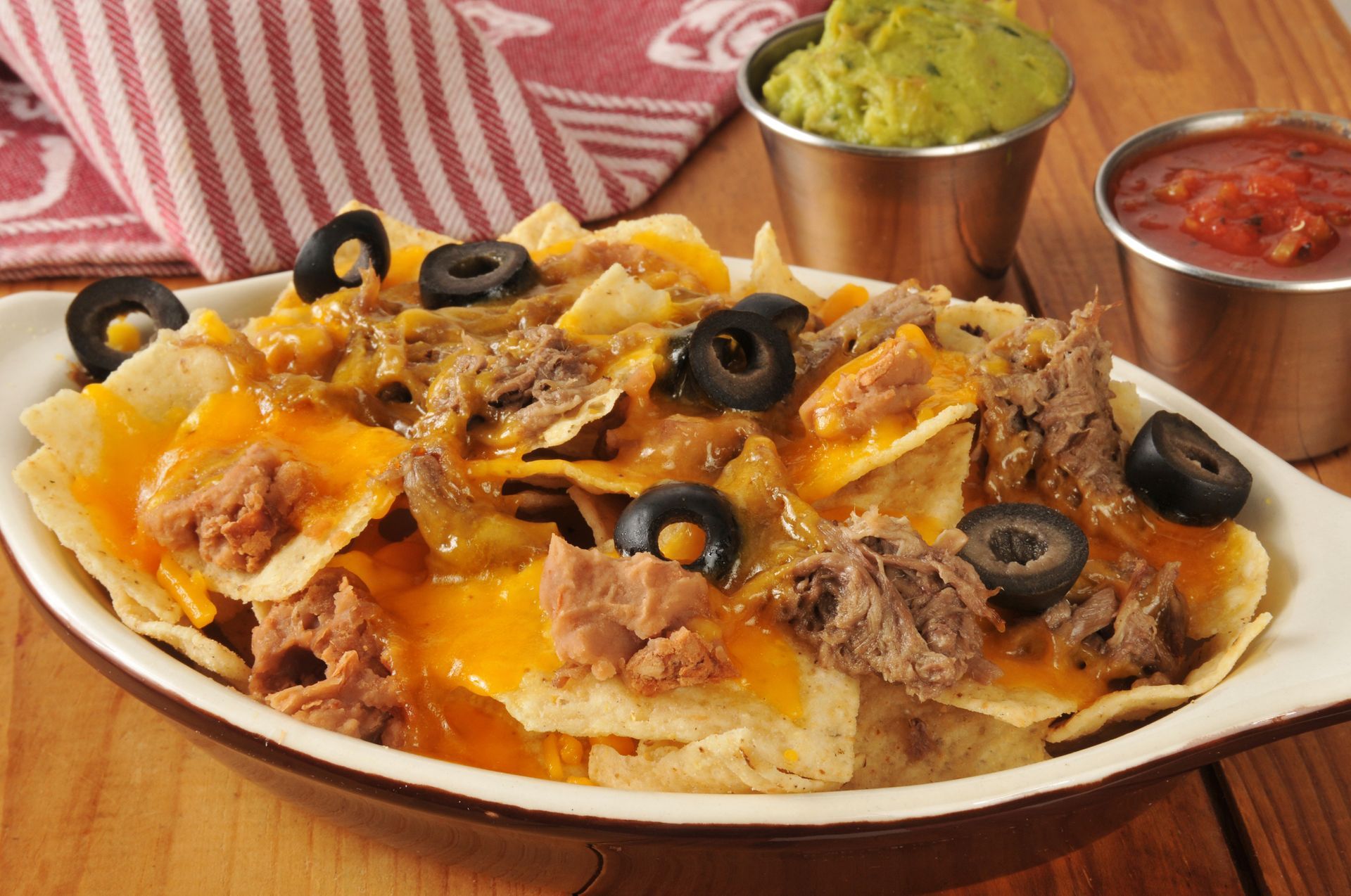 A casserole dish filled with nachos and guacamole on a wooden table