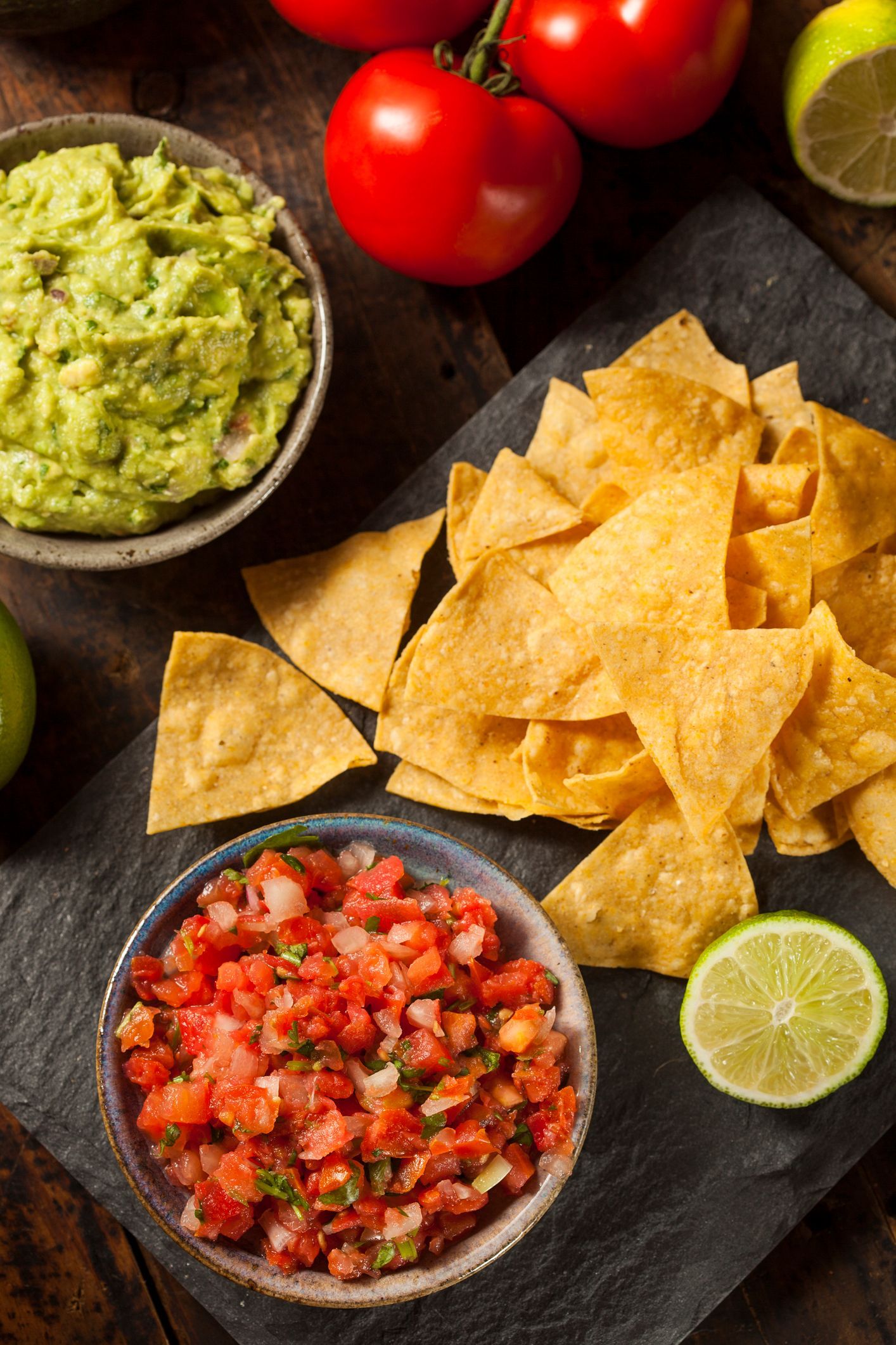 A bowl of guacamole, salsa, and tortilla chips on a cutting board.