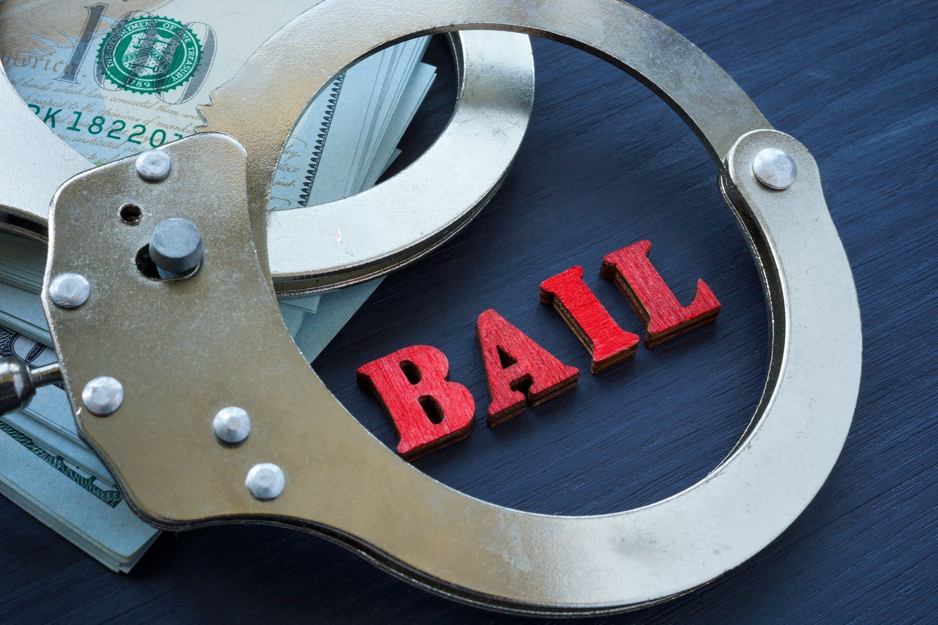 Handcuffs over a U.S. dollar bill with red “BAIL” text on a dark background.