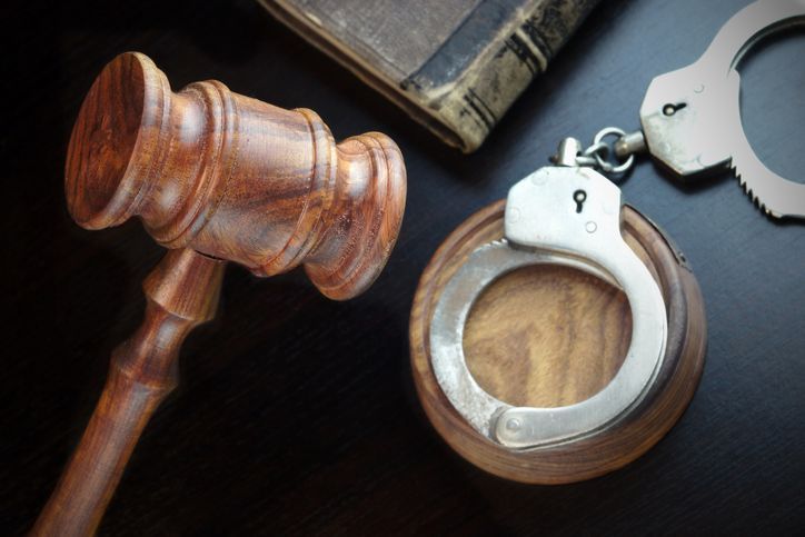Wooden judge’s gavel beside handcuffs on a dark surface.