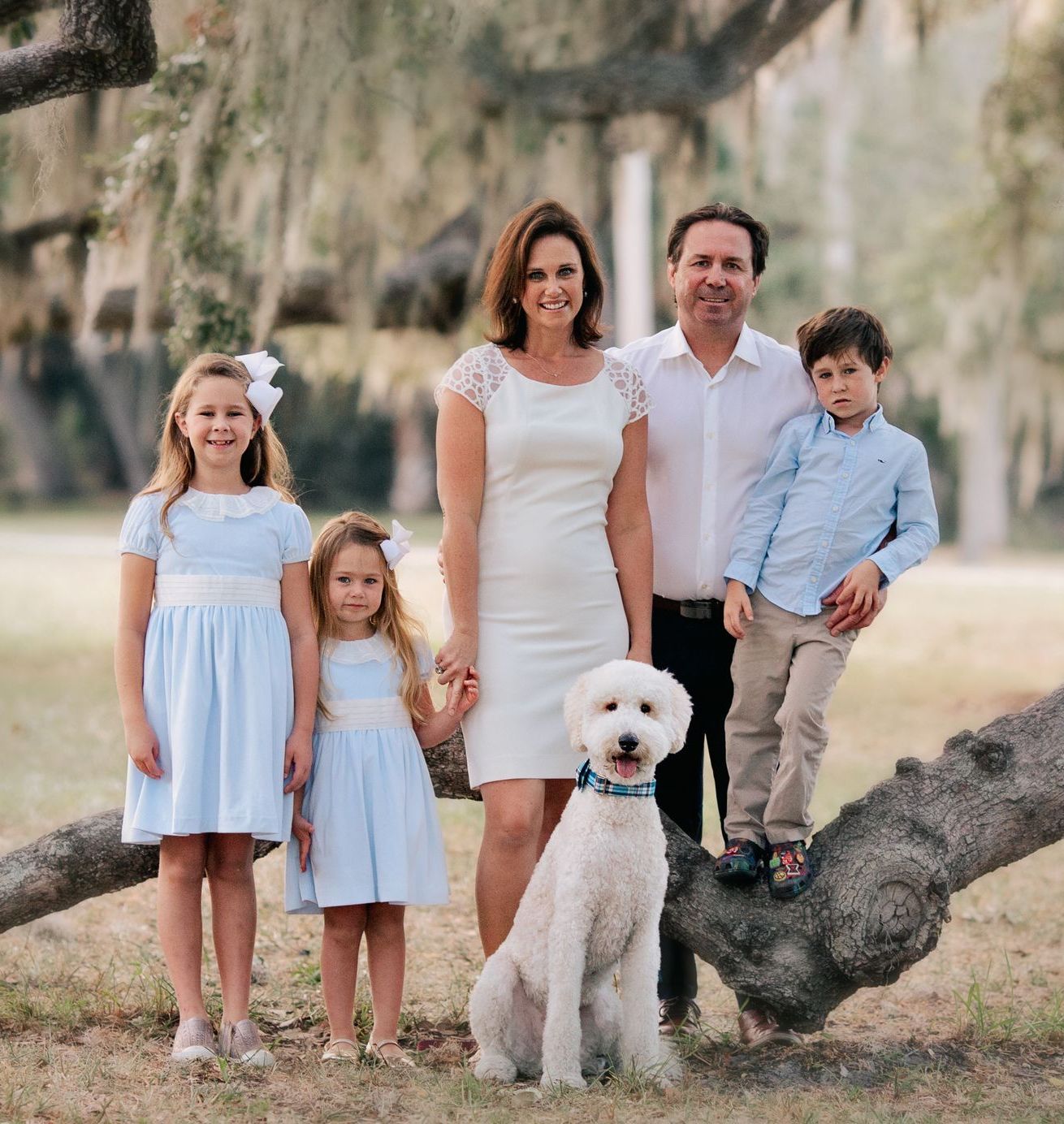 A family posing for a picture with a dog sitting on a tree branch.