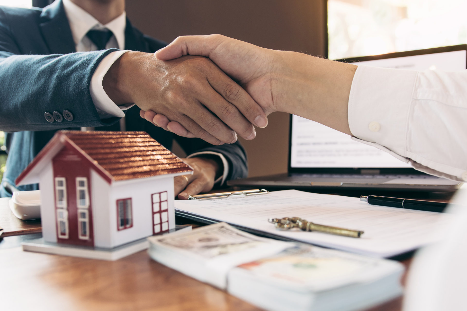 A man is shaking hands with a woman in front of a model house.