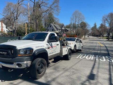 A white tow truck is towing a white car down a street.