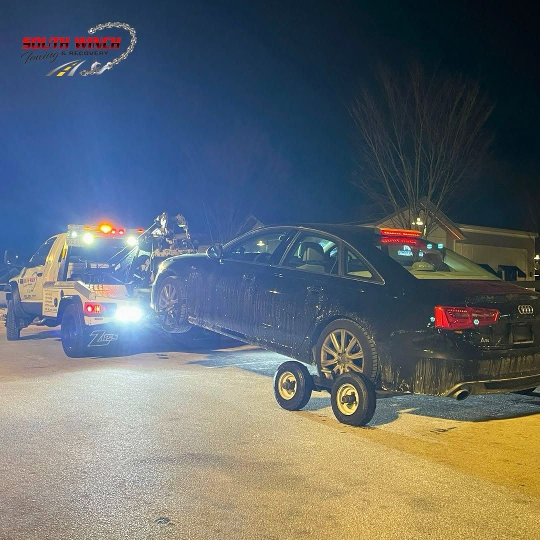 A car is being towed by a tow truck at night.