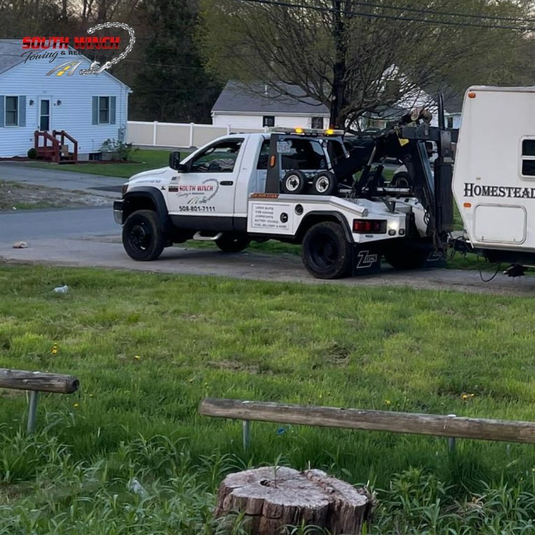 A white tow truck is towing a white car down a street.