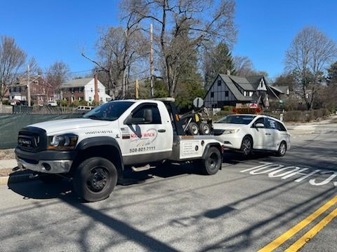 A white tow truck is towing a white car down a street.