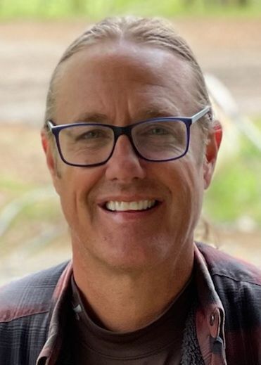 A man wearing glasses and a plaid shirt is smiling for the camera.