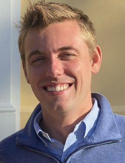 A man in a blue sweater is smiling for the camera.