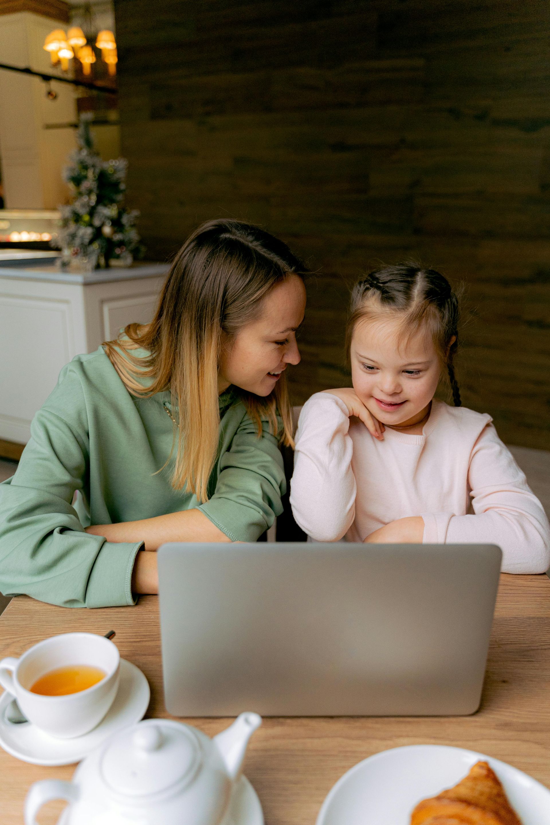 A woman and a little girl are sitting at a table looking at a laptop.