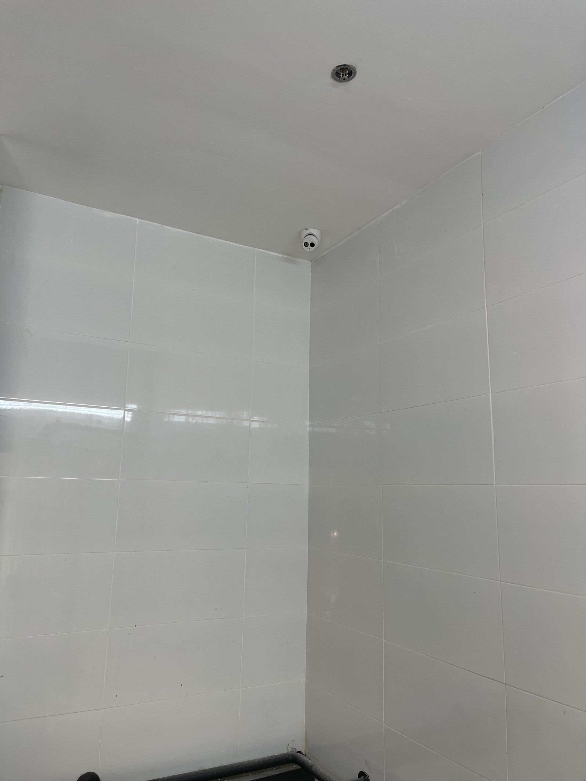 חדר אמבטיה עם אריחים לבנים ומצלמה על התקרה.