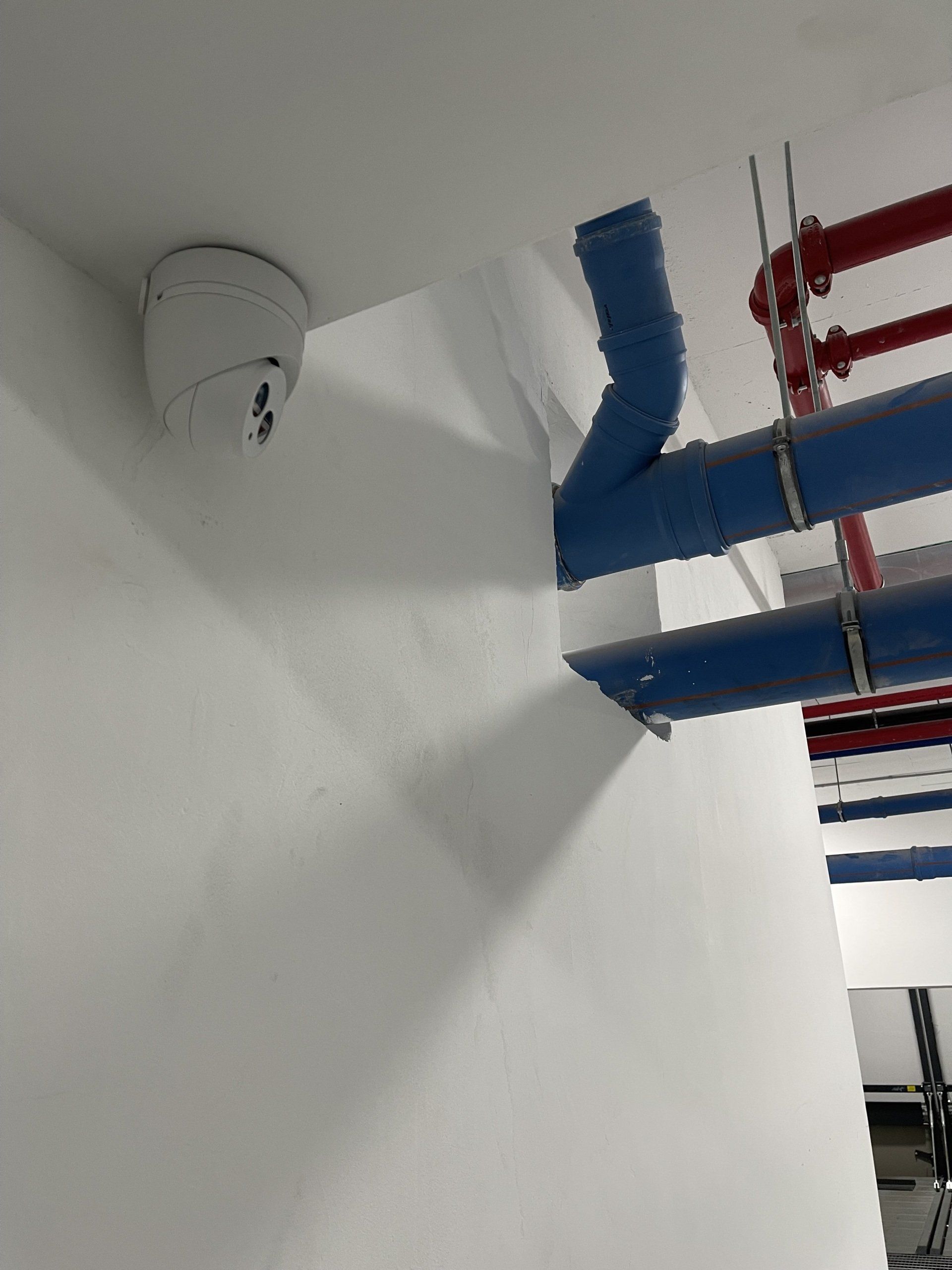 גלאי עשן תלוי מהתקרה ליד צינורות כחולים.