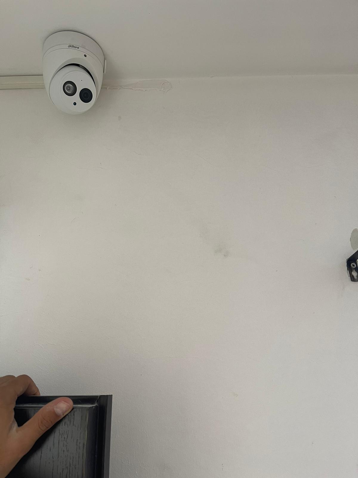 אדם מחזיק מסגרת תמונה מול קיר לבן ועליו מצלמה.