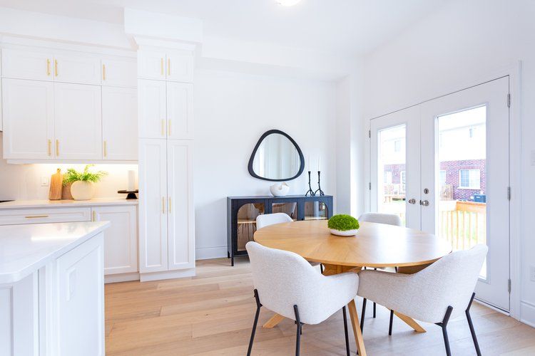 A dining room with a round table and chairs and a mirror on the wall.
