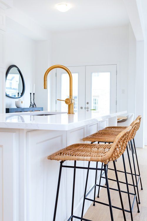 A kitchen with white cabinets , wicker bar stools , a sink and a mirror.