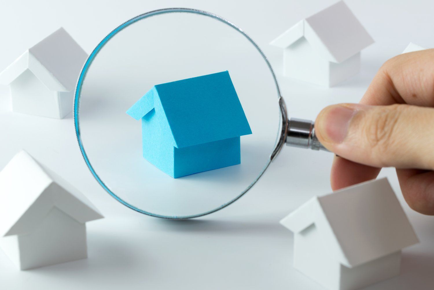 A person is holding a magnifying glass over a blue house