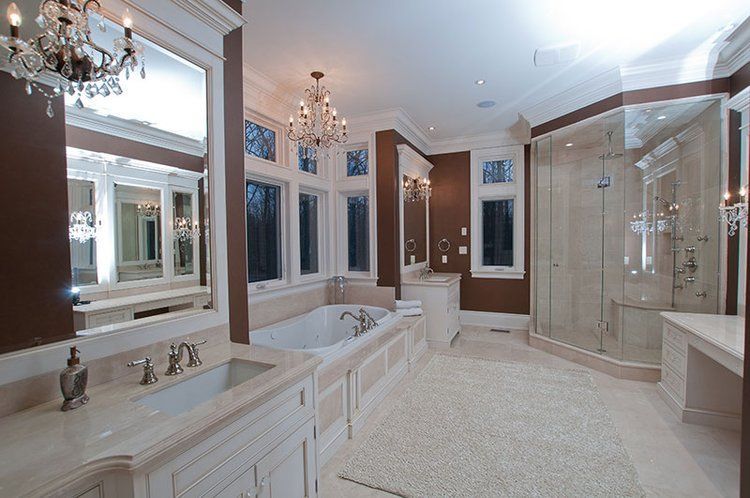 A bathroom with a tub , sink , mirrors and a chandelier.