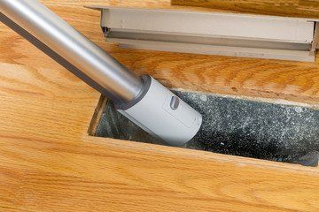 A vacuum cleaner is cleaning a duct in a wooden floor.