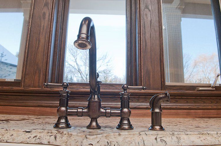 A kitchen sink with three faucets and a window in the background.