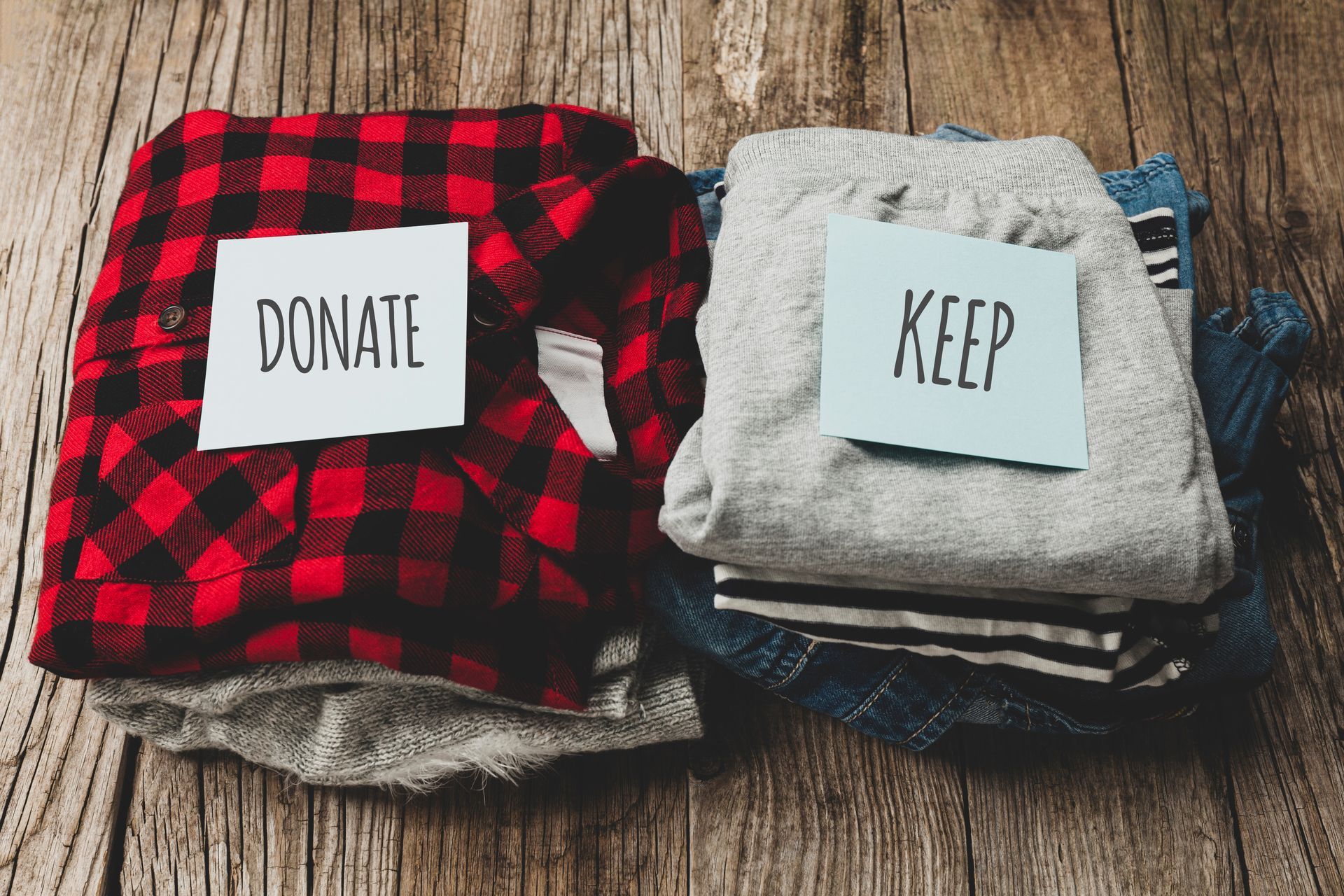 A pile of clothes with a donate and keep sign on a wooden table.