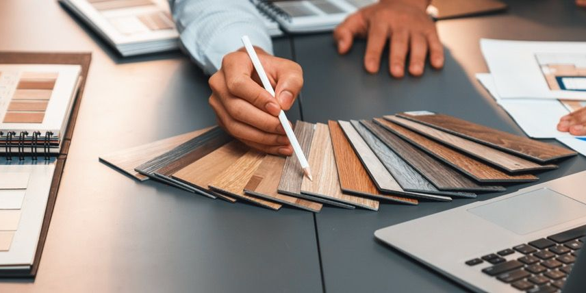 People around a table, choosing wood samples for a design project, with a laptop and floor plans.