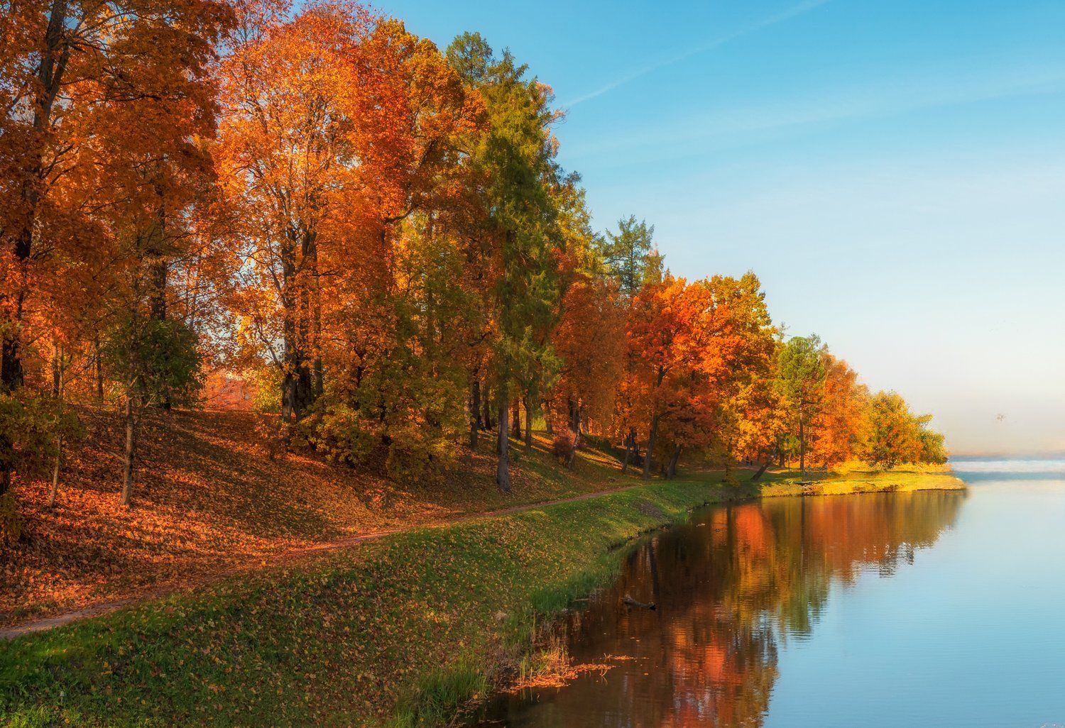 A lake surrounded by trees in autumn with a path leading to it.