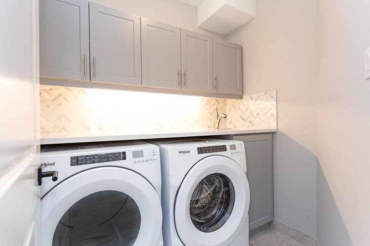 A laundry room with a washer and dryer and gray cabinets.