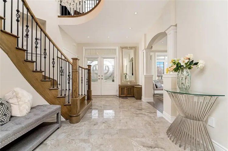 A hallway with stairs , a bench , a table and a vase of flowers.
