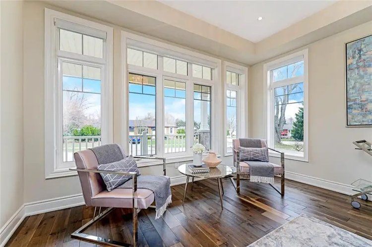 A living room with hardwood floors , chairs , a table and a lot of windows.