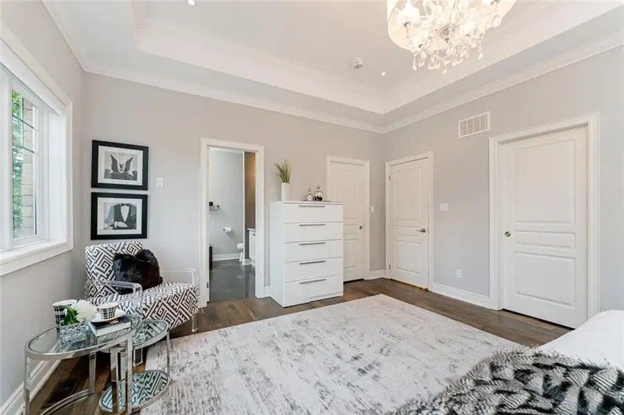 A bedroom with a bed , chair , dresser and chandelier.